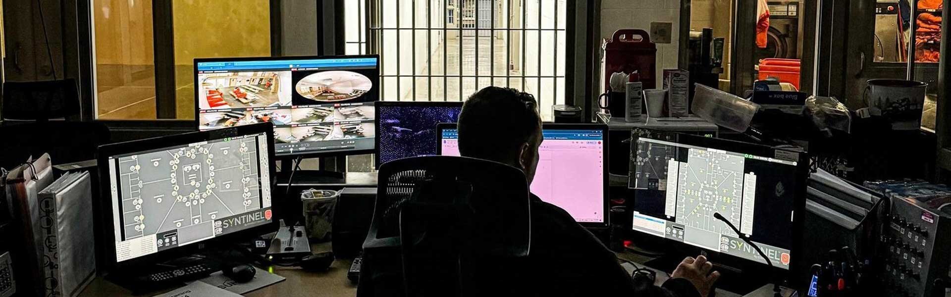 A man sitting at a desk in the jail looking at several computer screens
