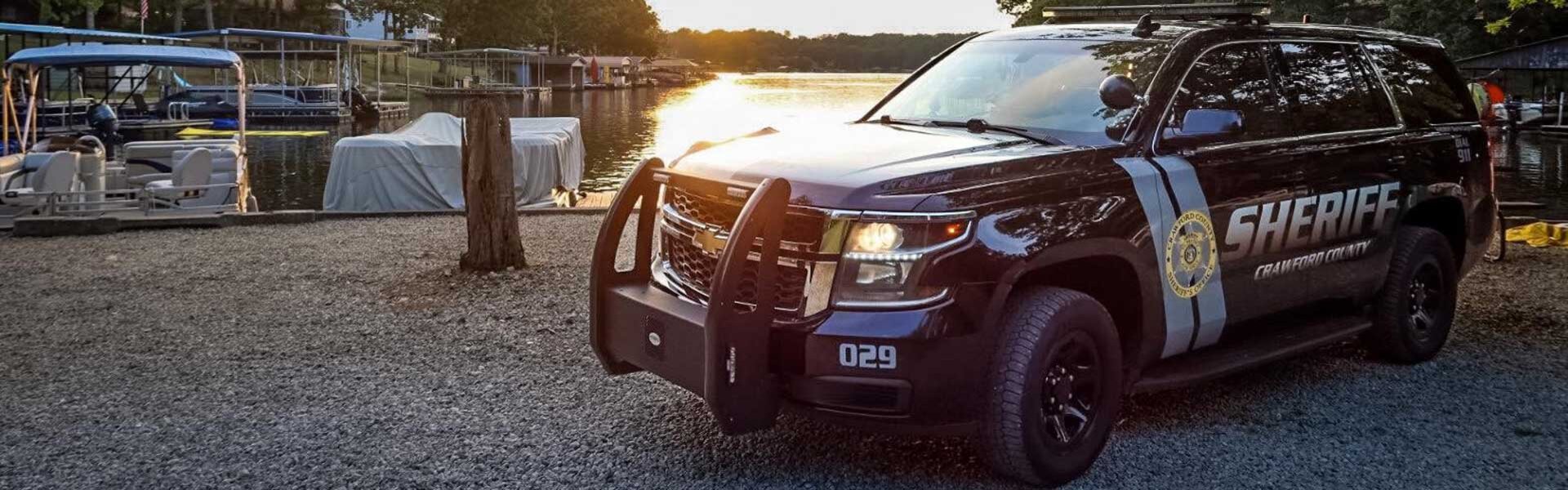 Sheriff patrol vehicle parked next to waterfont with several boats parked in the water